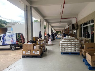 Hombre de pie junto a furgoneta PILADEX, mientras otros organizan cajas en un espacio de trabajo.