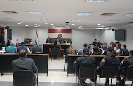 Sala de audiencias con tres miembros del tribunal y un oficial de seguridad, mientras ciudadanos observan atentos en ropa formal.