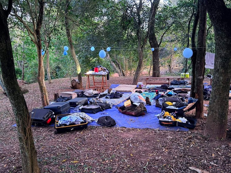 Mochilas y maletas sobre tela azul, con globos colgando entre árboles en un entorno natural claro.