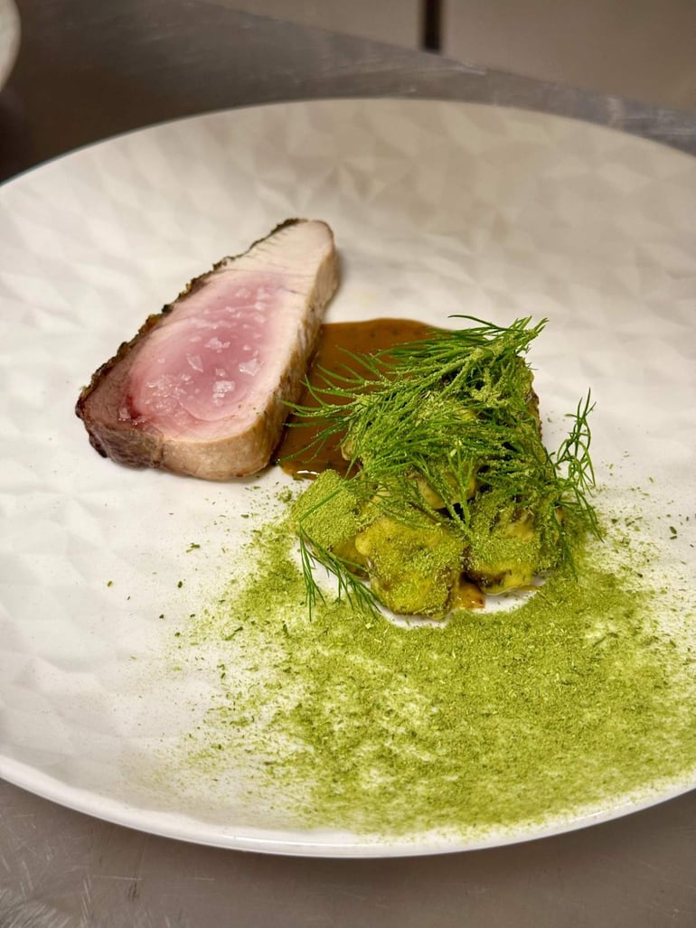 Plato de carne de cerdo rosa en el centro, salsa marrón y toque verde decorativo en una cocina elegante.