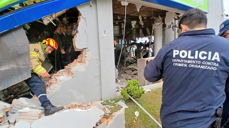 Bombero con casco rojo inspecciona escombros junto a un oficial de policía que observa los daños en edificio derrumbado.