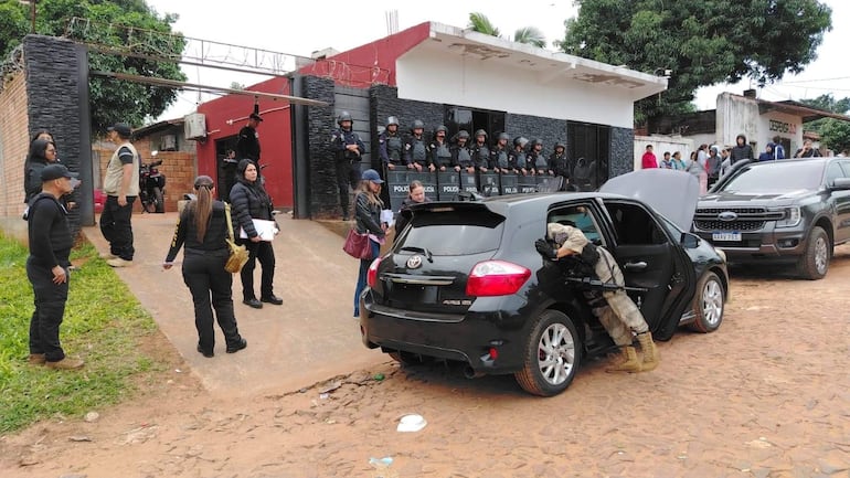 Grupo de policías en uniforme táctico y civil durante operativo, con un agente armado agachado junto a un vehículo negro.