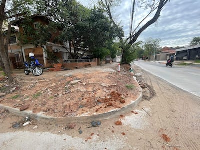 Motocicleta azul estacionada en terreno de obra, rodeada de escombros y árboles en una calle del barrio Santo Domingo.