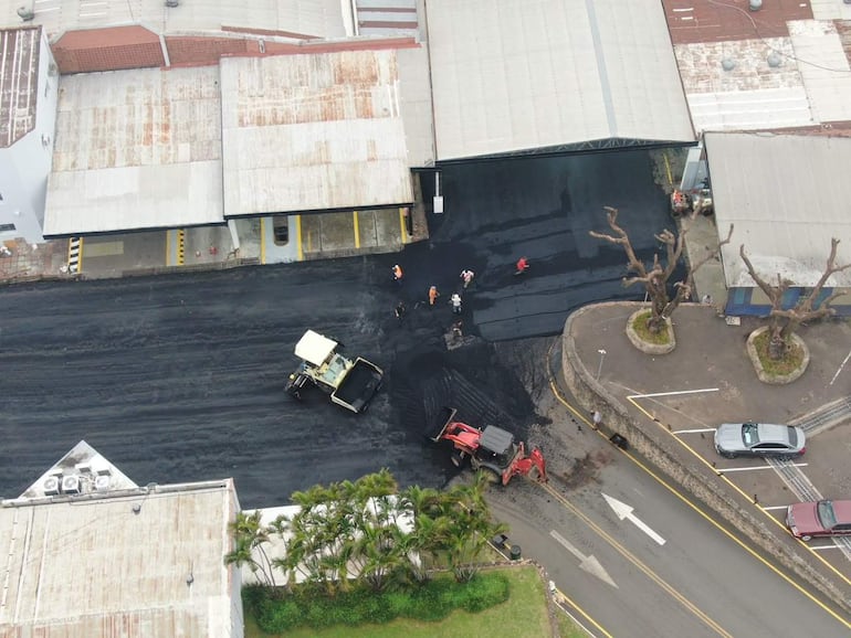 Trabajadores de vialidad en chalecos naranjas y camiseta roja, junto a maquinaria, pavimentan un área en Asunción.