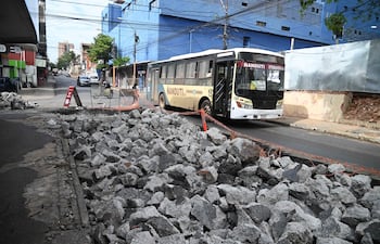 Ómnibus Nandutí navega entre piedras en una calle de Asunción, con un letrero de advertencia visible en el primer plano.