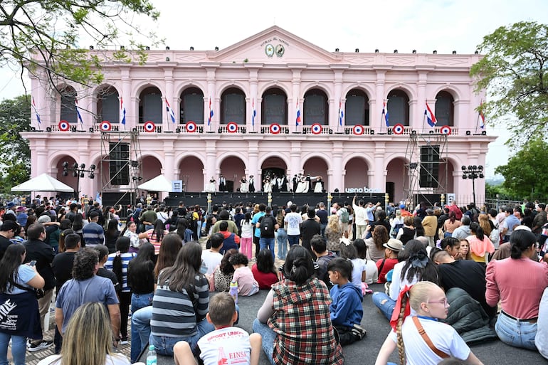 Multitud de personas en evento al aire libre, disfrutando de un concierto frente a un escenario con banderas paraguayas alrededor.