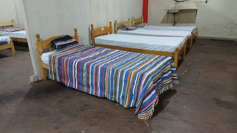 Interior de albergue con cinco camas. Manta de colores en la cama más cercana y sábanas blancas en otras.