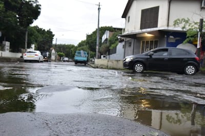 Calle suburbana inundada con dos vehículos parcialmente sumergidos, casas y vegetación alrededor, bajo un cielo nublado.