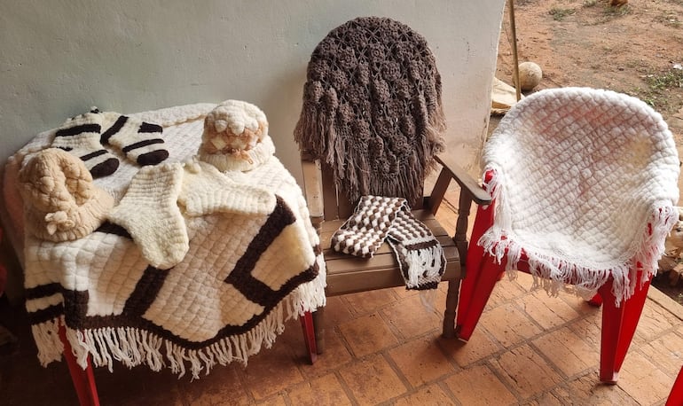 Ambiente al aire libre con sillas de madera y objetos textiles en tonos beige y marrón dispuestos sobre una manta.