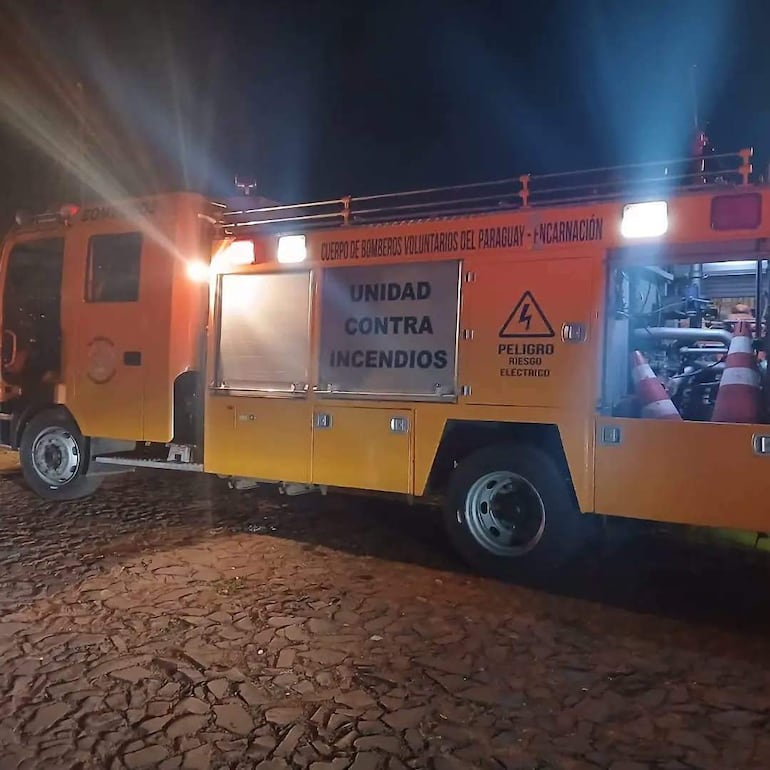 Camión de bomberos amarillo estacionado en calle empedrada, luces encendidas, sin personas visibles.