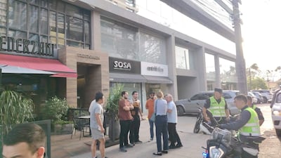 Dos mujeres en pantalones cortos y un grupo de hombres conversan en un ambiente urbano, mientras policías uniformados participan de la escena.