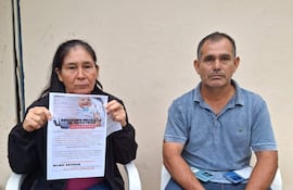 Mujer con chaqueta negra y hombre en camiseta azul, sentados con cartel de Benjamín, expresiones serias, en un ambiente público.