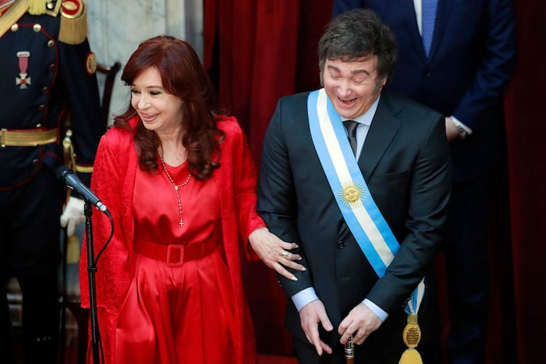 Cristina Fernández con cabello largo y rojizo, vestida de rojo, sonríe junto a Javier Milei con banda presidencial y atuendo oscuro.