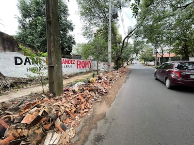 Calle con montículo de escombros y un coche burdeos transitando, grafitis visibles en muros de fondo.