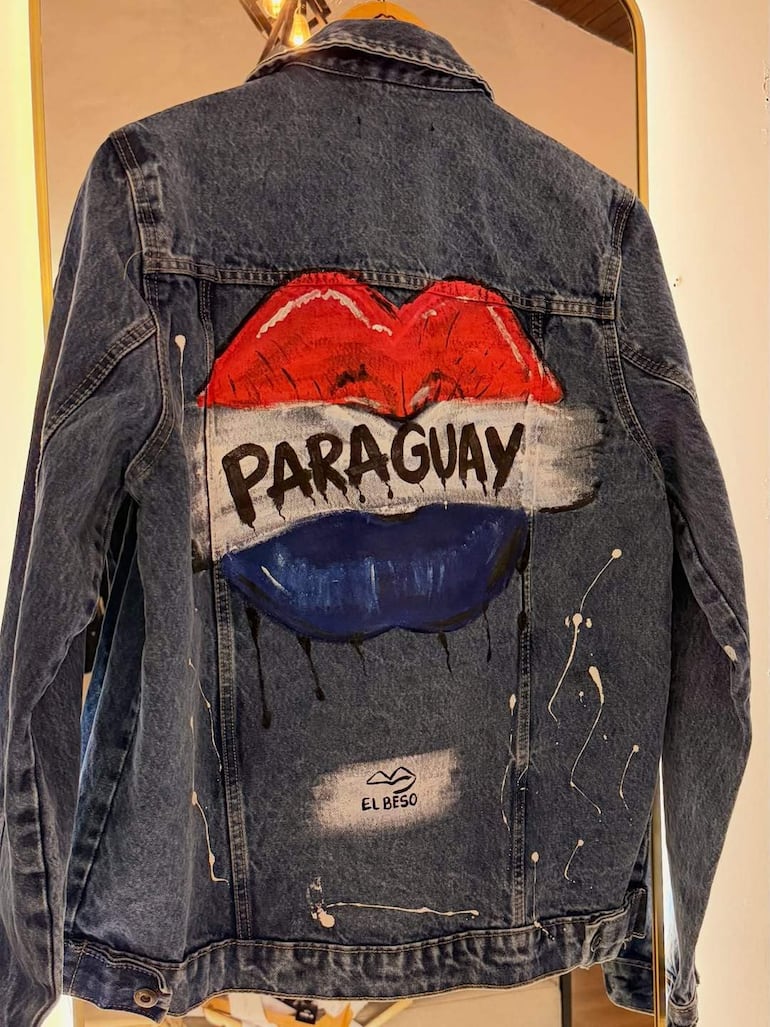 Chaqueta de denim en perchero con diseño de labios rojos y azules, palabras 'PARAGUAY' en franja blanca, en un entorno de exhibición.