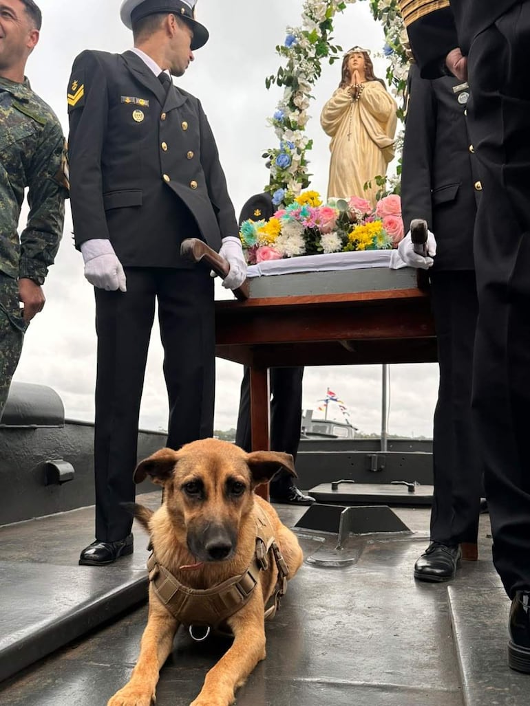 Hombres con uniforme militar y estatua religiosa en embarcación, con Maruca, un perro mestizo, en primer plano.