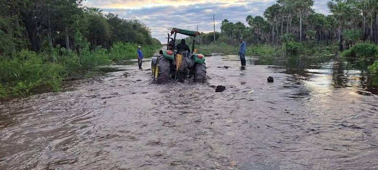Tres personas observan y guían un tractor en aguas, en camino inundado en Fuerte Olimpo en el 2025