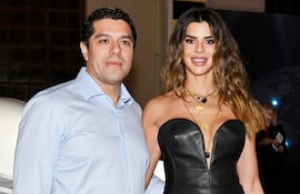Hombre de camisa blanca y mujer en atuendo negro de cuero y encaje, ambos sonriendo juntos en un evento.