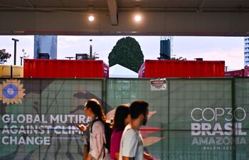 Personas caminan junto a generadores eléctricos que funcionan con diésel a las afueras del Centro de Convenciones Hangar donde se realiza la COP30, en Belém (Brasil).
