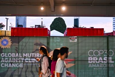 Personas caminan junto a generadores eléctricos que funcionan con diésel a las afueras del Centro de Convenciones Hangar donde se realiza la COP30, en Belém (Brasil).