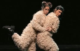 Paola Irún y Guadalupe Lobo en trajes esponjosos y claros, entrelazadas en el escenario oscuro durante una actuación.