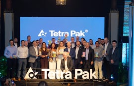 Gianmarco Felippo, rodeado de personas en trajes formales, sonríe en un evento con el logo de Tetra Pak de fondo.
