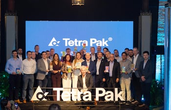 Gianmarco Felippo, rodeado de personas en trajes formales, sonríe en un evento con el logo de Tetra Pak de fondo.