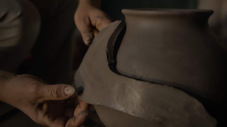 Manos trabajando en un recipiente de barro en un taller, resaltando la tradición de la cerámica paraguaya.