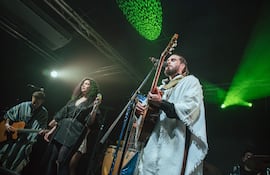 Vocalista en poncho blanco y mujer con micrófono en el centro, iluminados por luces verdes y amarillas, crean un ambiente vibrante.