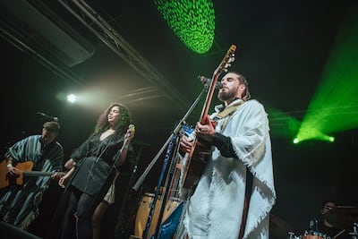 Vocalista en poncho blanco y mujer con micrófono en el centro, iluminados por luces verdes y amarillas, crean un ambiente vibrante.