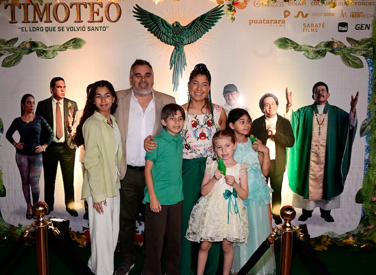 Mujer con blusa colorida y hombre en traje claro junto a tres niños sonrientes con vestimenta variada, en un ambiente festivo.