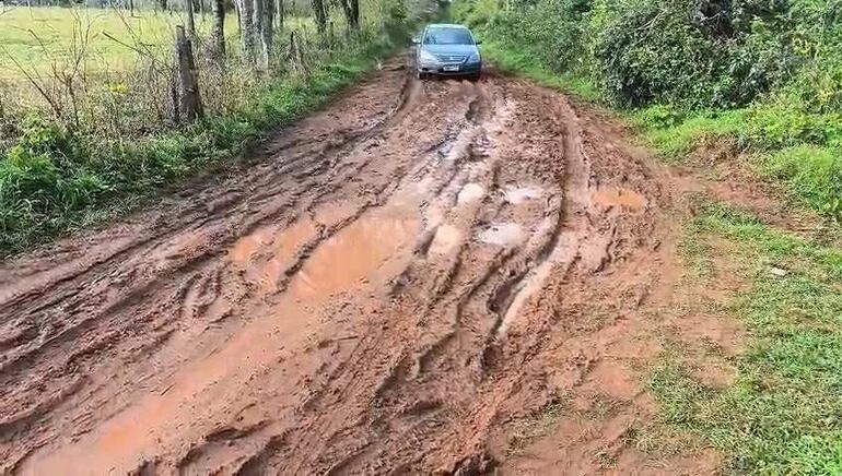 Automóvil gris circulando por un camino de tierra con surcos y charcos, rodeado de vegetación en la comunidad de Ibáñez Rojas.
