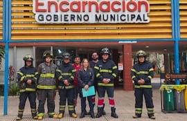 Cuatro bomberos en uniforme con cascos, una mujer sostiene documentos y un hombre más, frente a Gobierno Municipal de Encarnación.