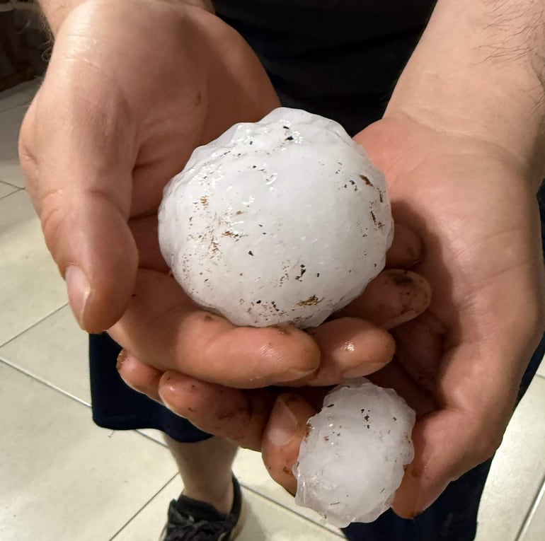 Persona sostiene grandes bolas de granizo, mostrando brazos musculosos y manos sucias de tierra, en un ambiente exterior.