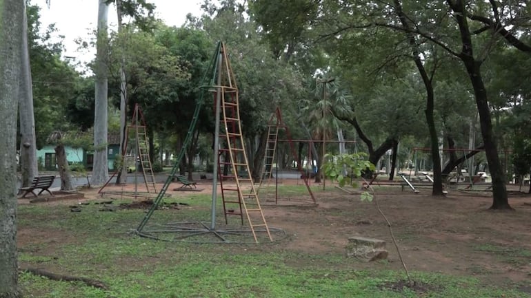 Parque Caballero sin personas, con estructuras de juego de colores y vegetación frondosa, en un ambiente desértico.
