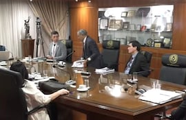 Manuel Ramírez Candia, en traje claro, abandona la mesa. Otras siete personas lo observan, en un ambiente formal.