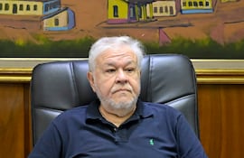 *Jorge Brítez, presidente de IPS Hombre canoso con barba, camiseta negra y pantalón claro, sentado serio en sillón de oficina con documento y bolígrafo frente a él.