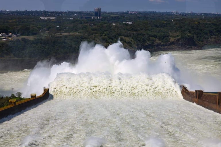 Cascada tumultuosa en el vertedero de Itaipú, rodeada de vegetación y edificios distantes.