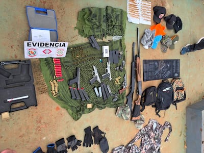 Mesa con armas, municiones y evidencias dispuestas en un entorno exterior desordenado.