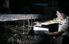 Hombre con camiseta de rayas y delantal, concentrado en manipular herramientas en un entorno oscuro con luz artificial.