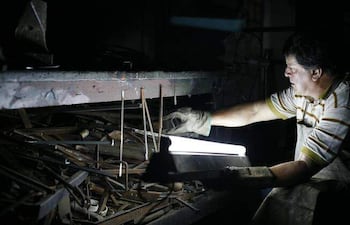 Hombre con camiseta de rayas y delantal, concentrado en manipular herramientas en un entorno oscuro con luz artificial.