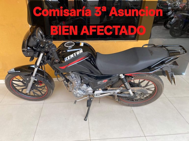 Motocicleta Kenton negra en comisaría con letreros visibles de 'bien afectado' sobre un piso de cerámica.
