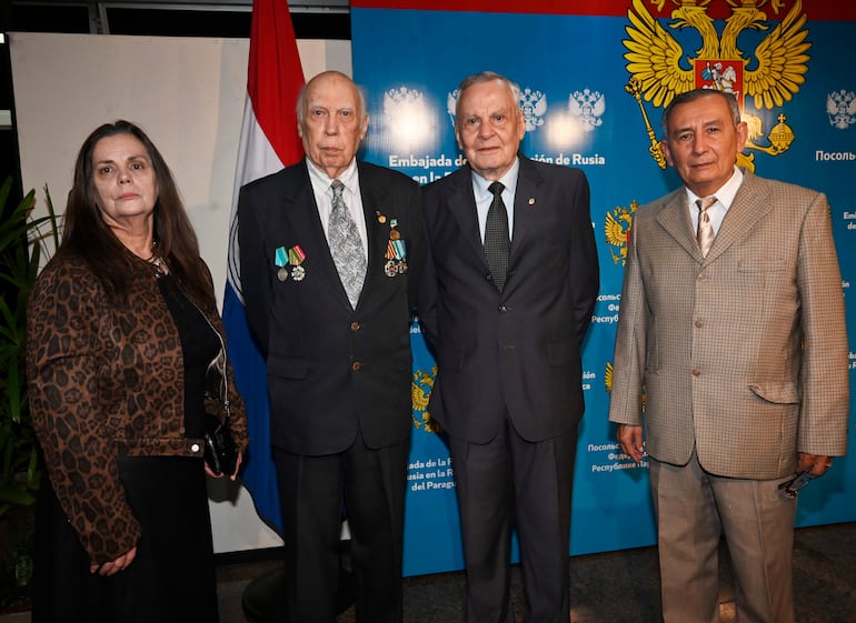 Dos hombres y dos mujeres, vestidos formalmente, posan en un ambiente institucional con bandera de Paraguay y símbolos rusos.