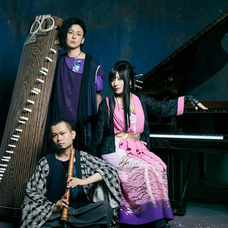 Mujer en kimono rosa en piano, hombre con flauta y otro con koto, en un ambiente musical oscuro.