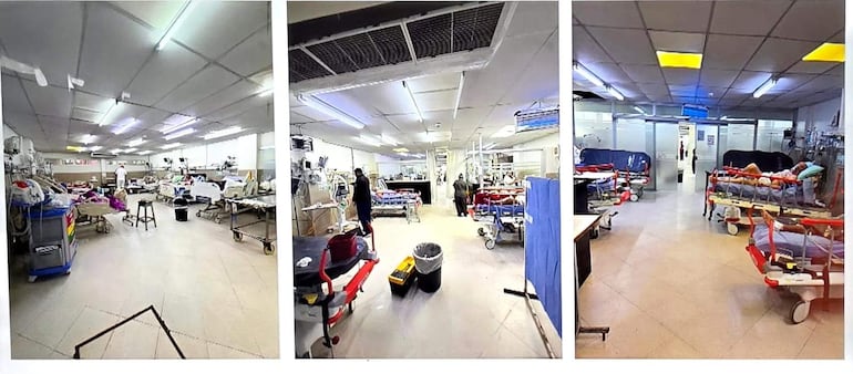 Médico en uniforme blanco atiende a paciente en cama, con otro trabajador de pie observando en el fondo de la sala de hospital.