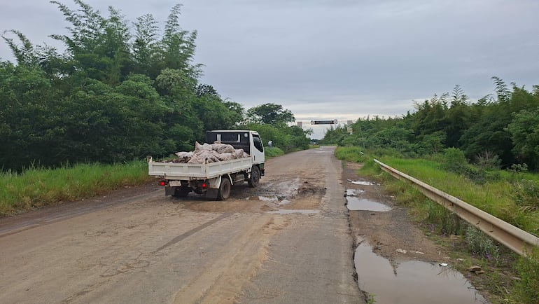 Camión blanco de carga circula por camino de tierra en mal estado, rodeado de vegetación densa.