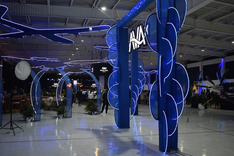 Ambiente festivo en el salón del aeropuerto, con arcos azules y mesas ocupadas por asistentes en un evento inaugural.