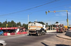 Camión de limpieza en movimiento en una intersección. Local 'Parador Tía Eli' visible con letrero rojo y logo de Coca-Cola.