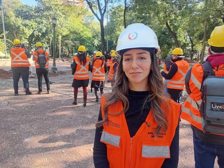 Arq. Verónica Martínez con chaleco naranja en primer plano, rodeada de trabajadores con chalecos y cascos amarillos en una obra exterior.