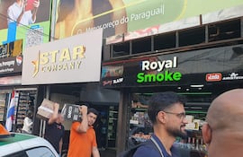 Hombre con camiseta naranja lleva cajas, mientras otro hombre vestido de negro interactúa en una zona comercial céntrica.